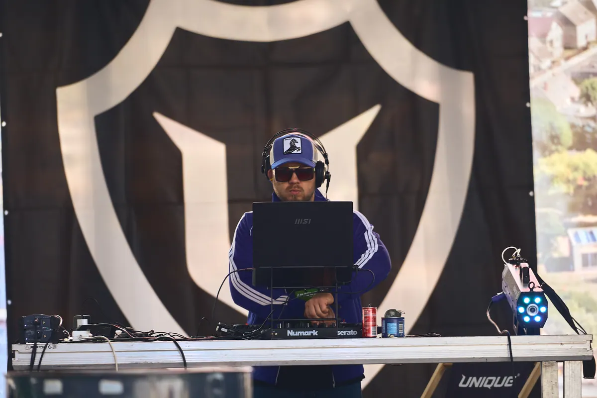 DJ przy konsolecie w świetle dnia, w tle baner z logo Unique Car Show