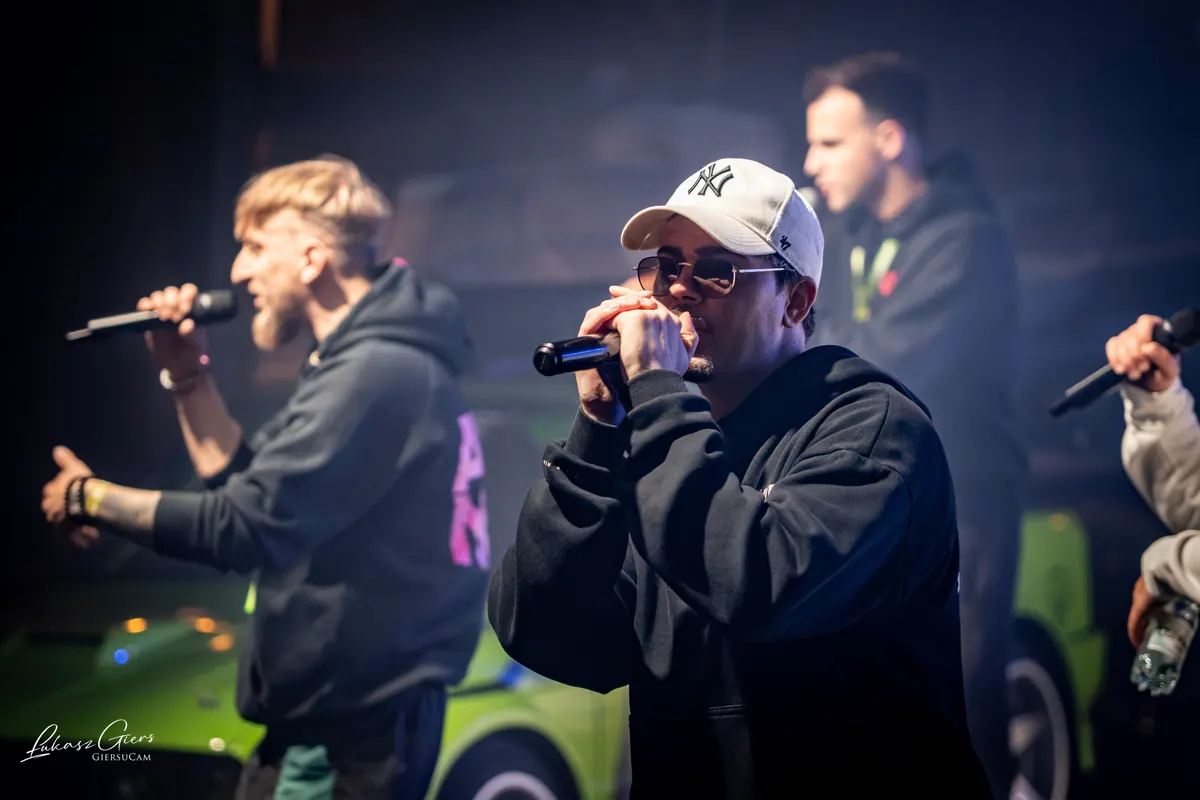 Dwóch wokalistów AVENEW z przodu sceny, za nimi zielony samochód UNIQUE