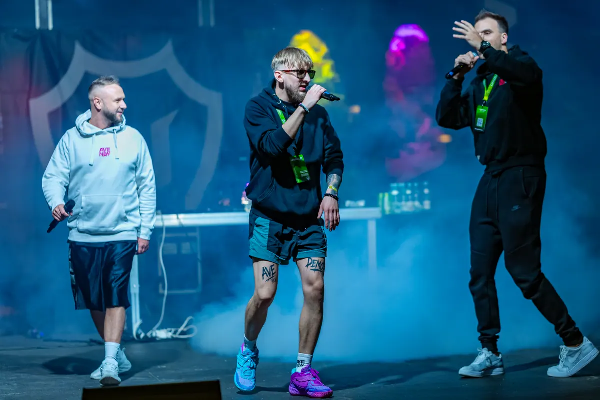 Trzej członkowie AVENEW na scenie w niebieskim dymie, wokalista w centrum kadru